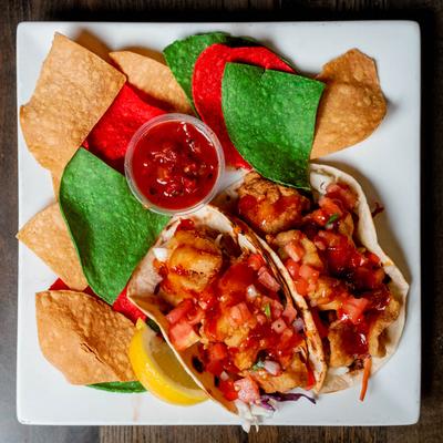 Fish tacos with salsa and tri-color tortilla chips on a white plate.