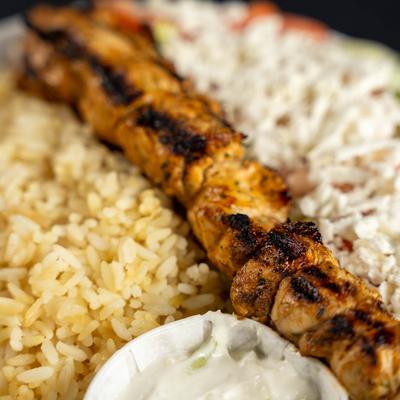 Chicken souvlaki over rice and chopped salad, served with a side of tzatziki sauce.