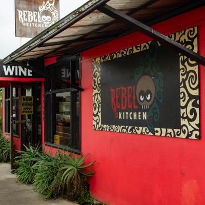 Exterior of Rebel Kitchen restaurant with a vibrant red wall and a painted logo.