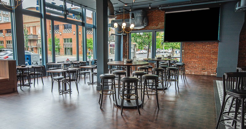 Interior of a modern cafe with large windows, round tables, and high stools.