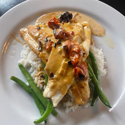 Fried fish fillet, smothered in sauce, on a bed of rice, with tomatoes, and green beansean