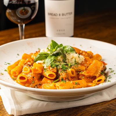 Rigatoni Bolognese served with a glass of red wine.