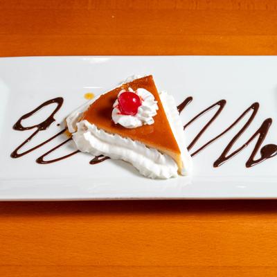 Slice of flan topped with whipped cream and a cherry.
