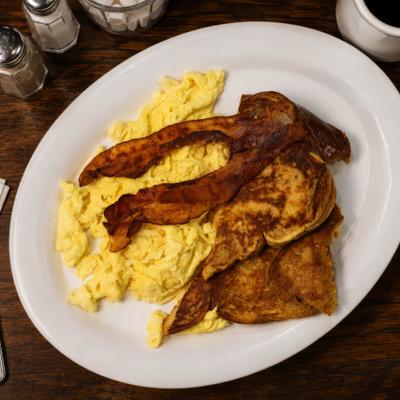 Scrambled eggs served with bacon strips and toasted bread.