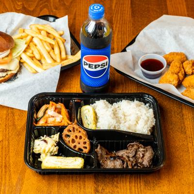 Bulgogi Bento Box served on the table with a bottle of soda, cheeseburger and chicken nugets.