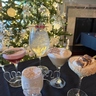 Various cocktails on a dark table with a decorated Christmas tree in the background.