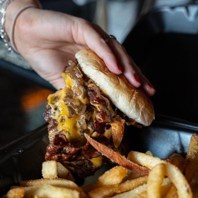 Hand lifting a bacon cheeseburger from a container with fries.