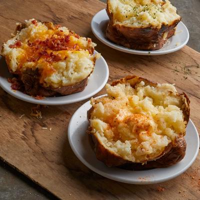 Three loaded baked potatoes on small white plates.