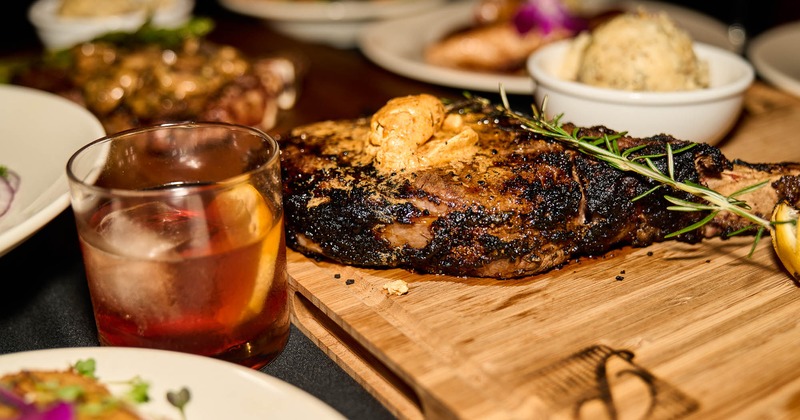 Porter house steak, Old Fashioned, and assorted food dishes, close up