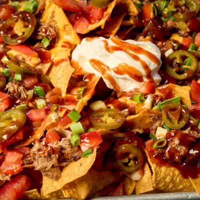 Smoked Pork Nachos, topped with jalapenos and sour creme, close-up.