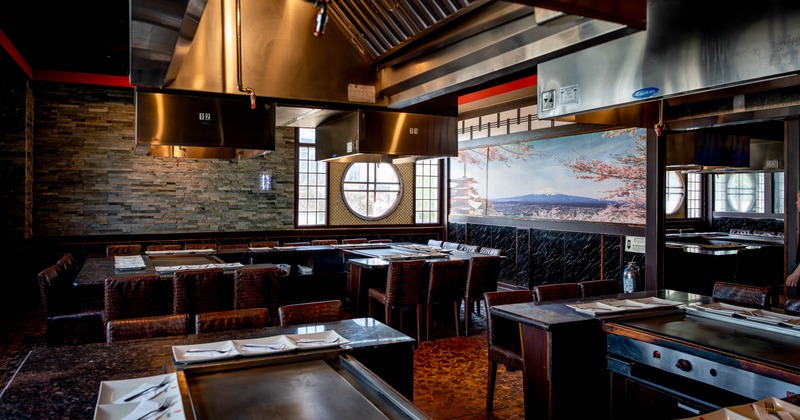 Interior of a teppanyaki restaurant with grills, seating, and a cherry blossom mural