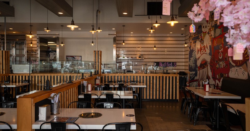 A modern interior with white tables, black chairs, pendant lights and a colorful mural