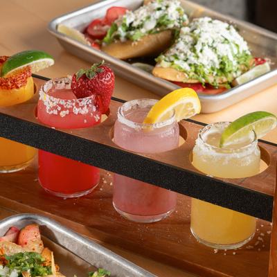 Margarita flight served on a wooden board alongside various meals.