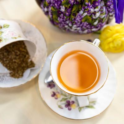 A cup of amber tea on a floral saucer next to loose tea.