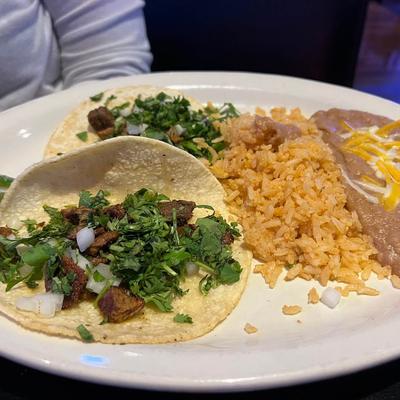 Carne asada tacos topped with cilantro and onions, served with rice and beans.