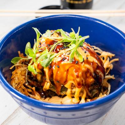 A vibrant blue bowl filled with glazed sushi rolls and crispy garnishes.
