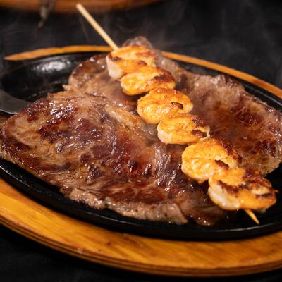Surf and turf dish featuring grilled steak and shrimp skewers, served in a skillet.