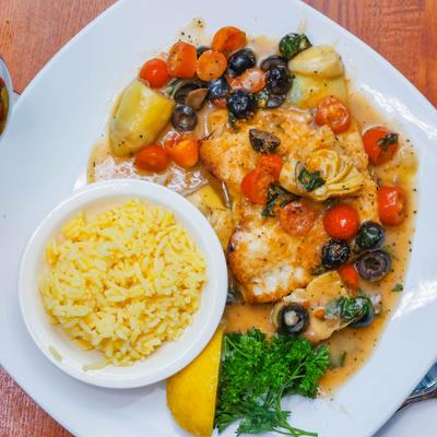 Chilean Sea Bass with cherry tomatoes, black olives, and rice on the side.