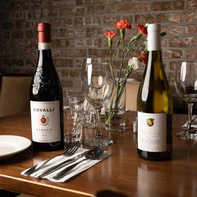 Two bottles of wine, empty wine glasses, and place settings sit on a wooden table.