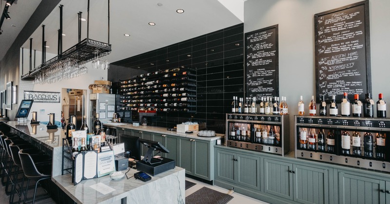 A modern wine bar - a marble countertop, wine bottles on shelves, hanging glassware.