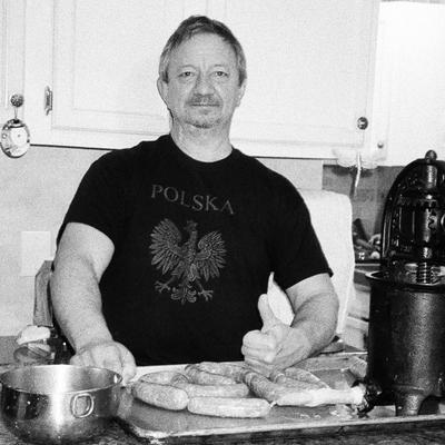 A person giving a thumbs-up beside freshly made sausages in a kitchen.