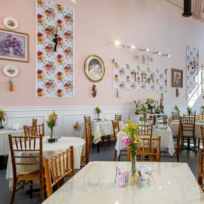Bright tea room with tables adorned with flowers, wooden chairs, and floral decor.