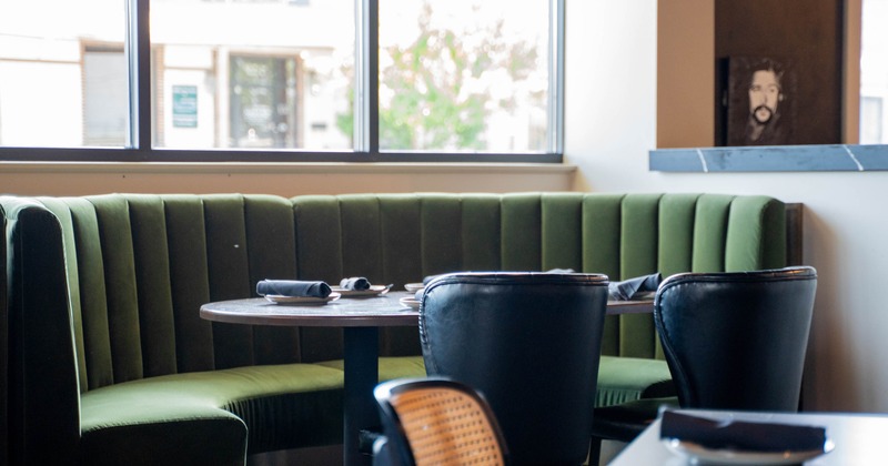 Green velvet booth with a round wooden table in a restaurant interior