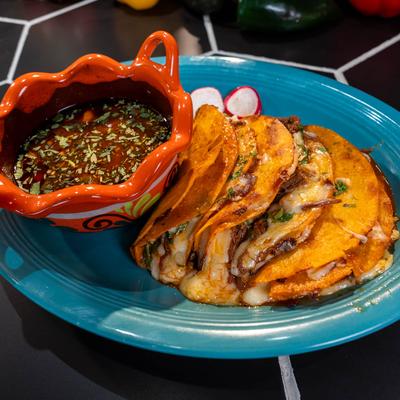 Birria tacos with birria dipping sauce on a blue plate.
