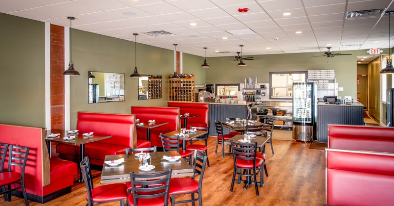Interior of a restaurant with red booths, tables and pendant lighting.