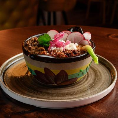A dish of tender steak, pork, and charro beans served in a bowl.