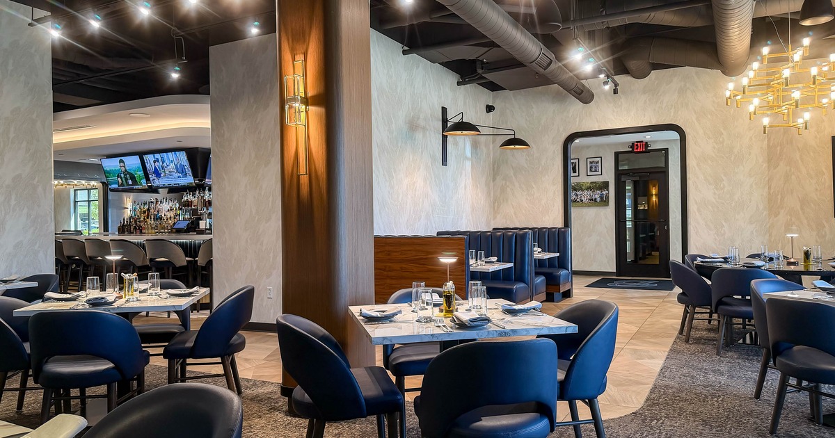 Modern restaurant interior with blue chairs and tables set for dining, featuring a bar area