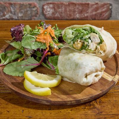 Chicken Caesar wrap with salad and lemon slices on a wooden board.