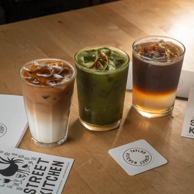 Iced Latte, Iced Matcha Latte, and Iced Cold Brew lined up on a wooden table.