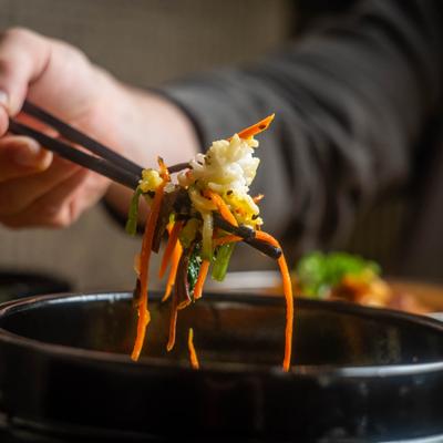 Hand taking bite of food from the bowl with chopsticks.