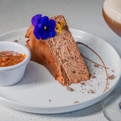 Chocolate mousse cake garnished with a purple flower, served with caramel sauce.