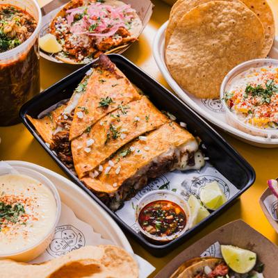 Quesabirria in a black plastic container, served alongside other dishes.