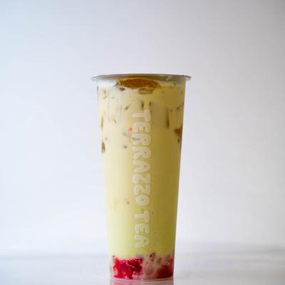 Tall clear cup of milk tea with ice and visible Terrazzo Tea logo, red fruit pieces at the bottom.