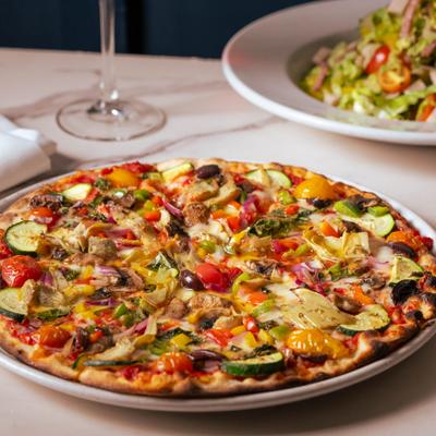 Loaded vegetable pizza topped with zucchini, artichokes, bell peppers, and tomatoes.