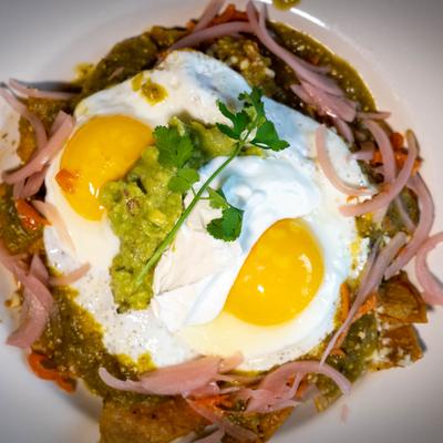 Chilaquiles with two fried eggs, guacamole, and pickled onions.