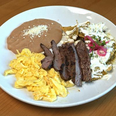 Tortilla chips smothered in green sauce, with steak strips, scrambled eggs, and beans.
