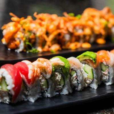 Two sushi rolls are displayed on dark plates, one colorful and one crispy.