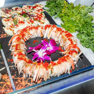 Decorative ring-shaped sushi platter garnished with orchids and red sauce.