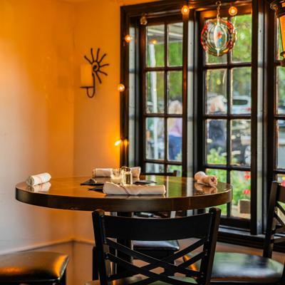 Restaurant interior with a round table, black chairs, and a large window overlooking a street scene.