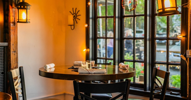 Interior, restaurant corner with a round wooden table set for four, near large windows