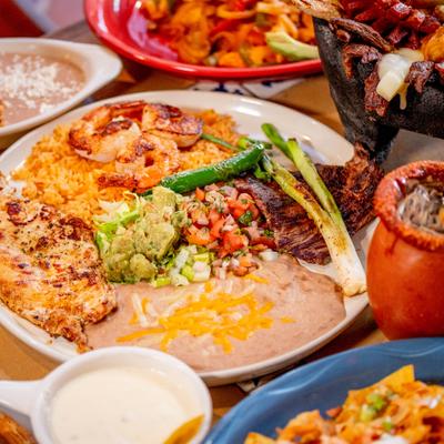 Grilled chicken, shrimp, steak, rice, beans and guacamole on a round plate.