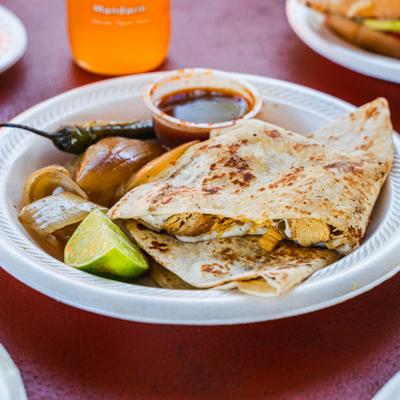 Chicken Quesadillas served with grilled onions, lime wedges, and a small container of salsa.