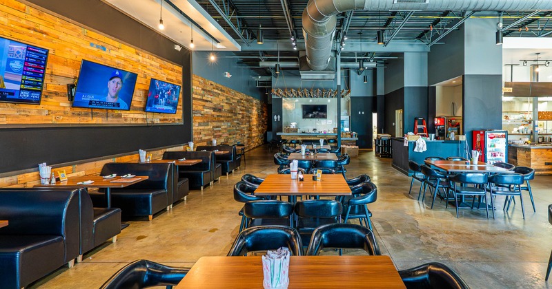 Interior with wooden tables, black chairs, booth seating, and multiple TVs on a reclaimed wood wall