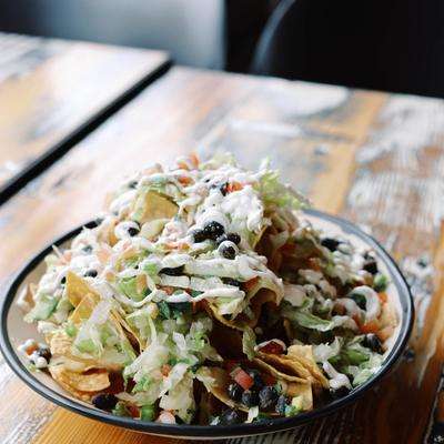 Loaded nachos topped with lettuce, black beans, tomatoes, and creamy dressing.