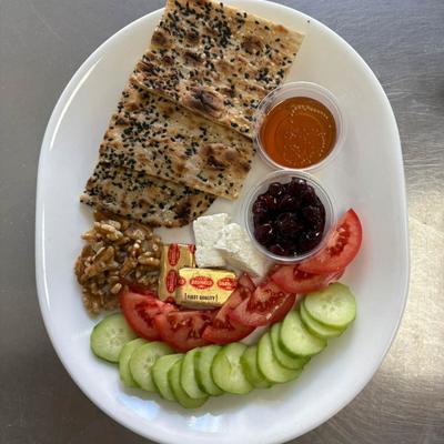 A plate featuring an assortment of food, including bread, cucumbers, tomatoes, jelly, butter.