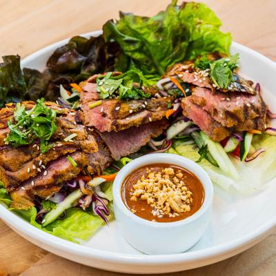 Beef satay wraps with lettuce, cabbage, and carrots, served with peanut sauce.